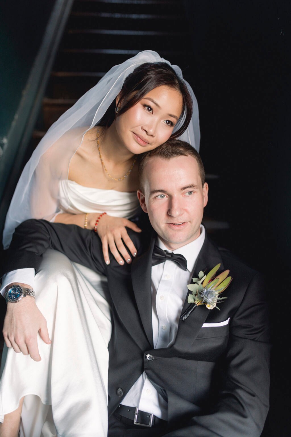 Bride Eda in her veil with her groom on a dark staircase, bridal makeup by Tian Soon