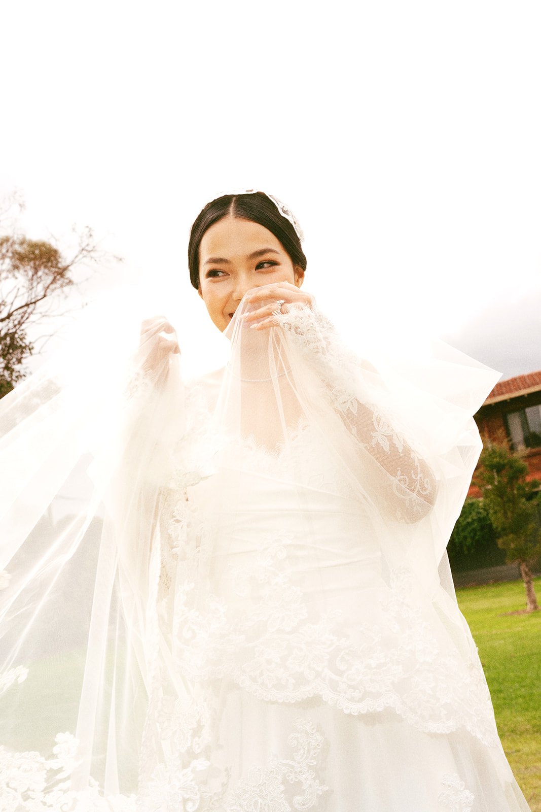 Bride laughing behind her veil in the garden, bridal makeup by Tian Soon