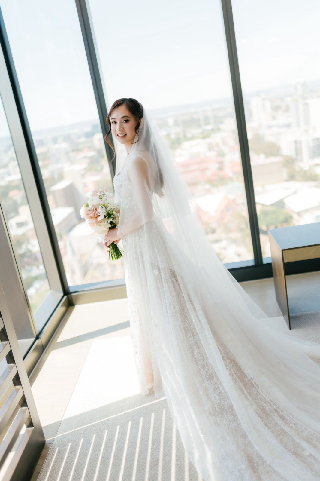 Bride Natalie in her veil by a sunlit window, bridal makeup by Tian Soon